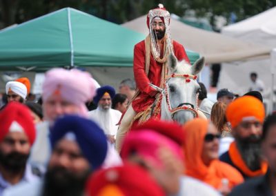 Man riding a white horse surrounded by people wearing Sikh turbans